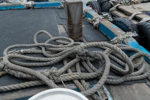 Coiled rope rests on a boat deck beside wooden pilings Stock Photos
