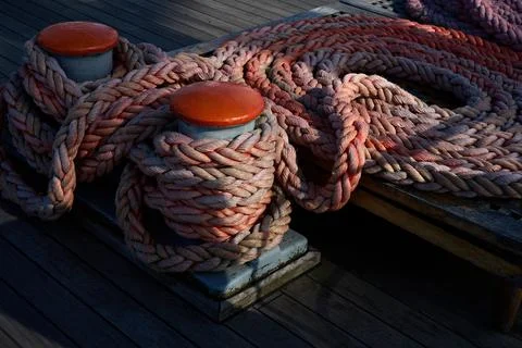 Coiled thick mooring ropes secured around metal deck bollards on wooden vesse Stock Photos