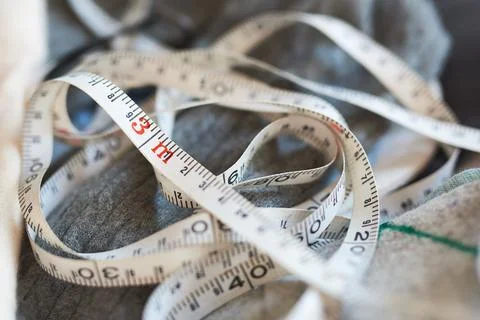 Coiled white tailor measuring tape placed over grey fabric during garment fit Stock Photos