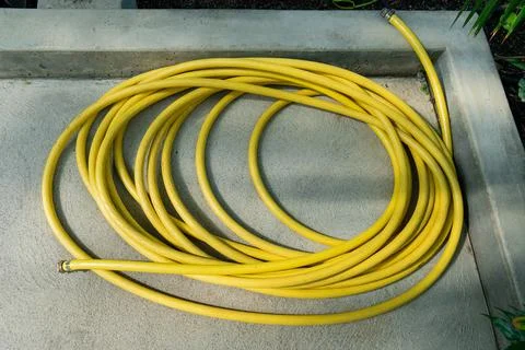 Coiled yellow material on concrete surface, ready for garden maintenance. Stock Photos