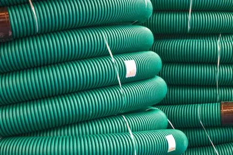 Coils of new red plastic pipe for underground cable protection with rain drops Stock Photos