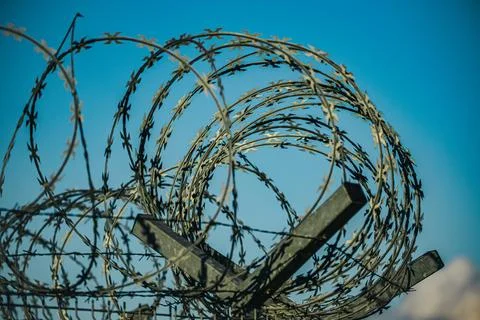 Coils of razor wire above a security fence against vivid blue sky with clou.. Stock Photos