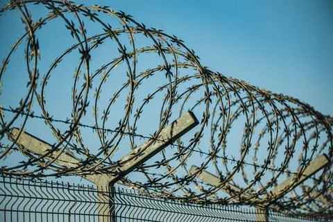 Coils of razor wire mounted on angled supports above a security fence again.. Stock Photos