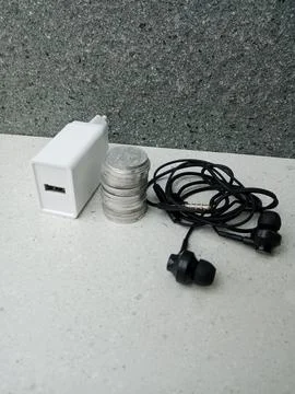 Coin Stack with Reversed Charger Head Facing Camera and Wired Headset Nearby Stock Photos
