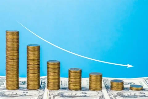 Coin stack step down graph on the background of banknotes with white arrow. Stock Photos