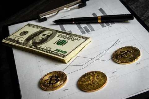 Coins in the form of bitcoin with a bundle of dollars on sheets of statistics Stock Photos