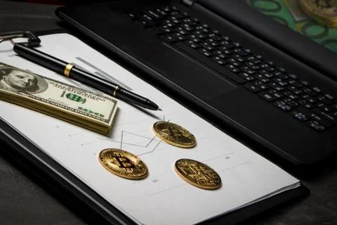 Coins in the form of bitcoin with a bundle of dollars on sheets of statistics Stock Photos