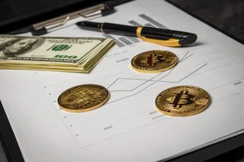 Coins in the form of bitcoin with a bundle of dollars on sheets of statistics Stock Photos