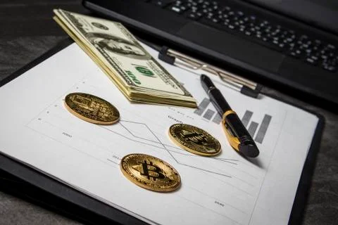 Coins in the form of bitcoin with a bundle of dollars on sheets of statistics Stock Photos