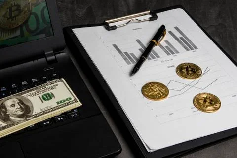 Coins in the form of bitcoin with a bundle of dollars on sheets of statistics Foto stock