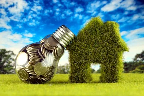 Coins inside the light bulb and miniature house with grass. Green eco renew.. Stock Photos