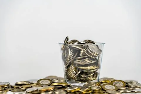 Coins inside a plastic container. Coins scattered on white background. Stock Photos