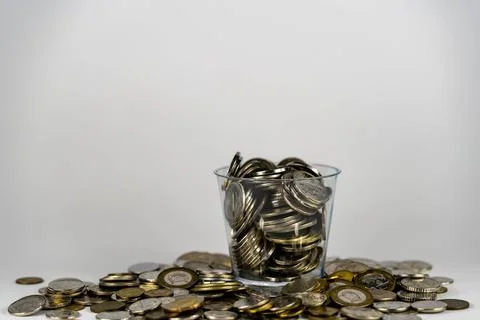 Coins inside a plastic container. Coins scattered on white background. Stock Photos