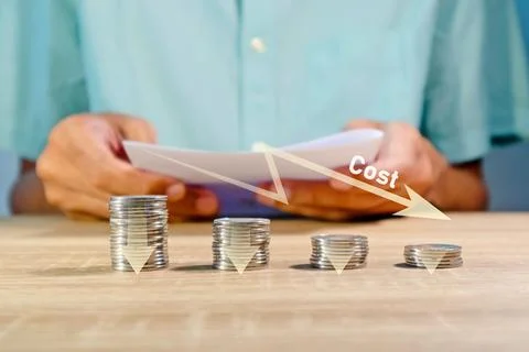 Coins stacking with the down arrow and man holding a paper to review the co.. Foto stock
