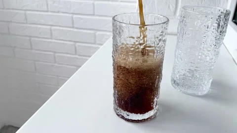 Cola with bubbles and thick foam is poured into a large faceted glass Stock Footage 312932973
