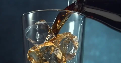 Cola pouring into glass with ice cubes in slow motion on blue background Stock Footage 346225965