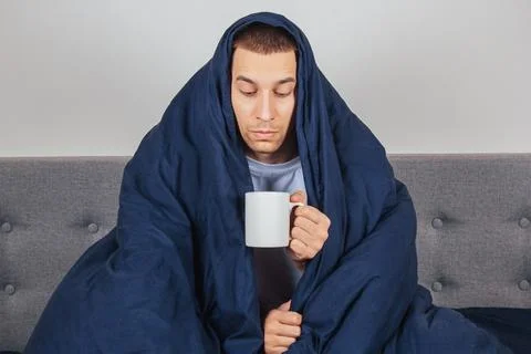 Cold and flu. Portrait of a sick young guy drinking tea in bed, sick caucasian Stock Photos