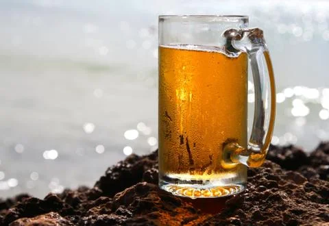 Cold beer cider glass on a cliif, shiny sea background Stock Photos