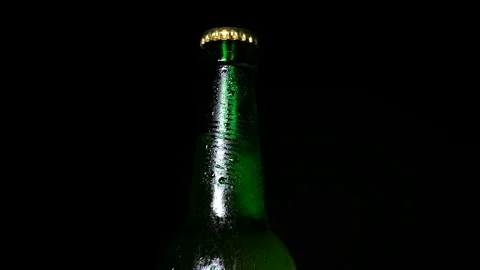 Cold beer with water drops on bottle is illuminated by light from the darkness Stock Footage 155798083