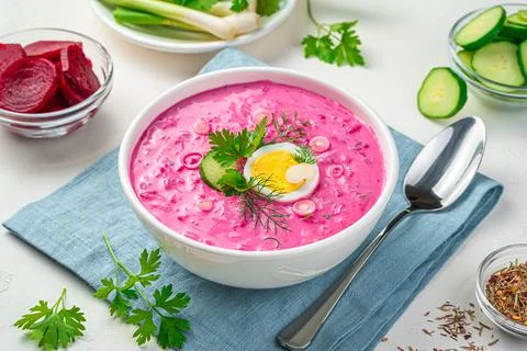 Cold beetroot soup with cucumber, egg and fresh herbs on a gray background. Stock Photos