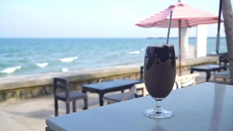 Cold black drink with straw on a table near the sea Stock Photos