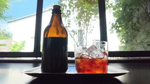 Cold brew coffee bottle and iced glass sit by sunlit window Stock Footage 344746812