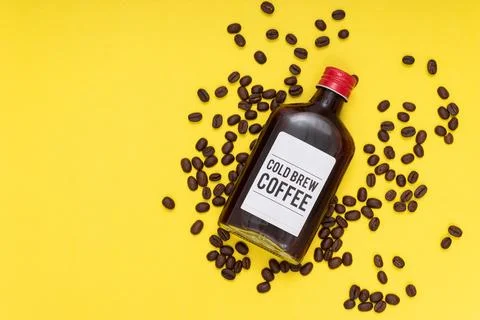 Cold brew coffee bottle with coffee beans, yellow background, flat layout Foto stock