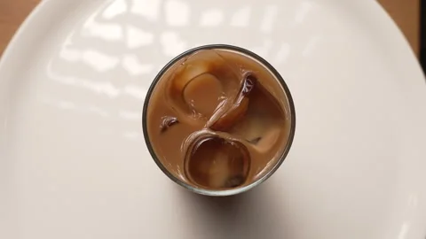 Cold brew coffee with milk and ice cubes spinning in a glass on a white plate Stockbeeldmateriaal 339152909