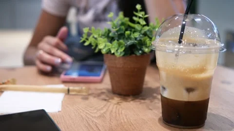 Cold brew coffee in plastic cup on table woman in background looking at phone Vidéo 280305593