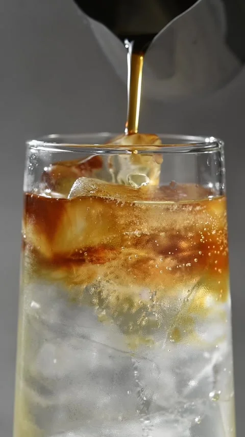 Cold brew coffee pours over ice into apple cider and tonic as dark coffee layers Stock Footage 345487199