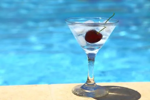 Cold cocktail with ice cubes and cherry by poolside Stock Photos