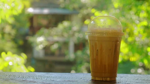 Cold coffee drink in plastic cup with lid on wooden table, set against Stock Footage 292818185