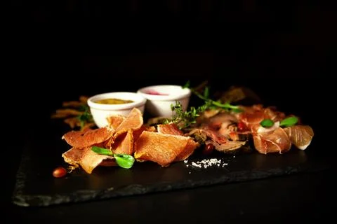 Cold cuts appetizer with herbs and sauces on a dark background in the restaurant Stock Photos