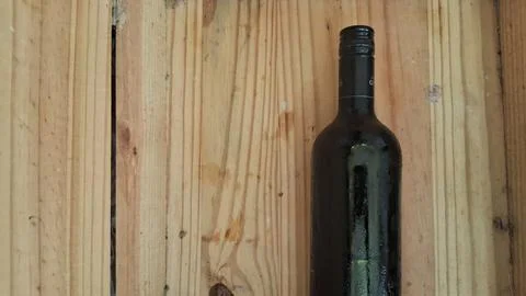 Cold dark wine bottle resting on a rustic wooden background surface Stock Photos
