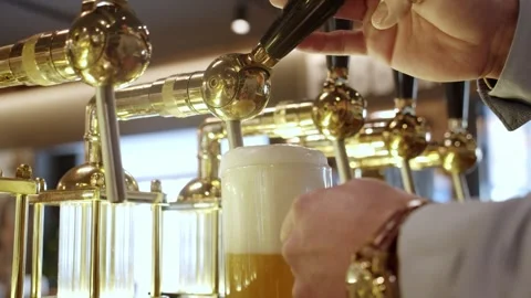 Cold draft beer with creamy head pulled from brass taps in public bar, low Stock Footage 272427428