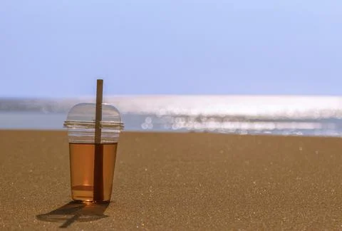 Cold drink in a plastic cup at the background of blurred sea, sand and blue sky Foto stock