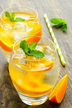 Cold drinks with ice and mint. Orange cocktail on rustic wooden table Stock Photos