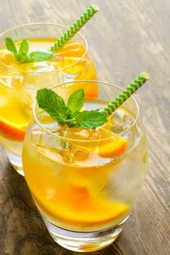 Cold drinks with ice and mint. Orange cocktail on rustic wooden table Stock Photos