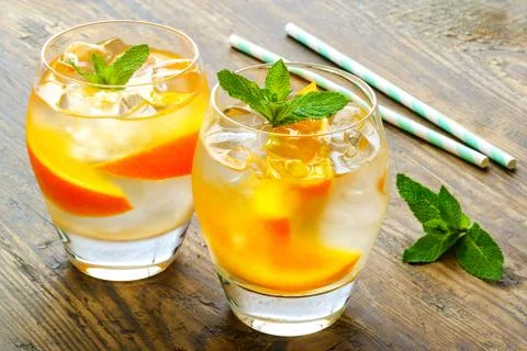 Cold drinks with ice and mint. Orange cocktail on rustic wooden table Stock Photos