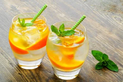 Cold drinks with ice and mint. Orange cocktail on rustic wooden table Stock Photos