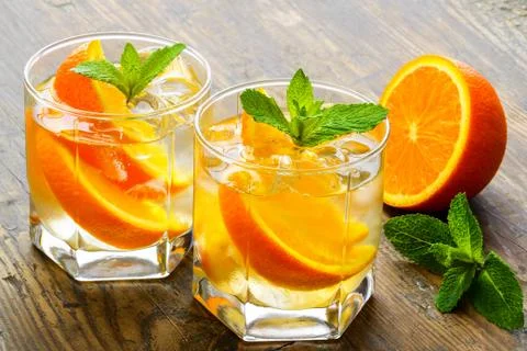Cold drinks with ice and mint. Orange cocktail on rustic wooden table Stock Photos