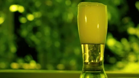 Cold glass of beer with foam standing on a table in a garden Stock Footage 340356008