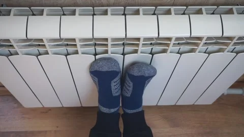 Cold home. A man warms his frozen feet on a white radiator at home Stock-Footage 318072017