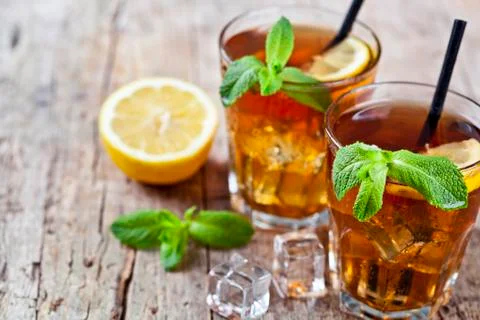 Cold iced tea with lemon, mint leaves and ice cubes in two glasses on rustic  Stock Photos