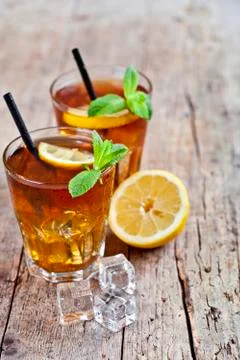 Cold iced tea with lemon, mint leaves and ice cubes in two glasses on rustic  Stock Photos