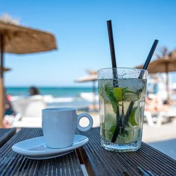 Cold mojito and coffee on the table in the sunny beach Stock Photos