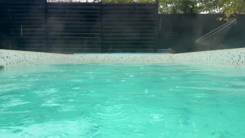 Cold raindrops creating circles on the surface of a steaming hot swimming pool Video stock 319483921