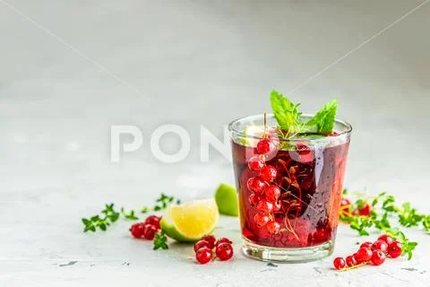 Cold red cocktail with currant, lime, mint, thyme and ice in glass on light g Stock Photos