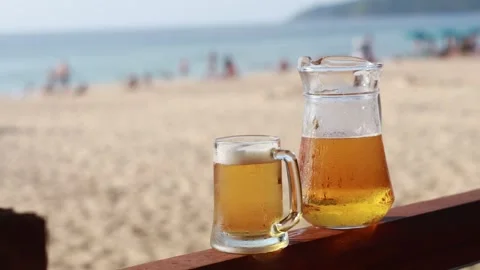 Cold refreshing beer pitcher and mug on a wooden railing overlooking a sand.. Stock-Footage 334326938