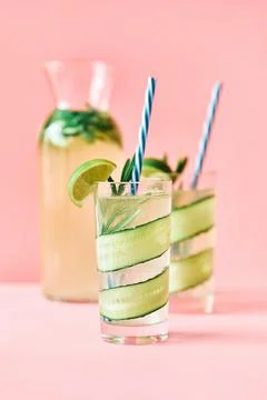 Cold refreshing cocktail with lime, cucumber, rosemary and ice in glass on pink Stock Photos